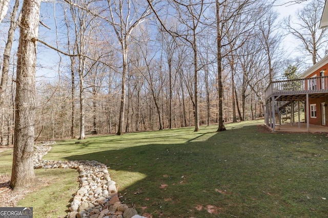 view of yard featuring a patio area, a wooden deck, and a view of trees