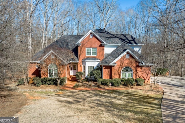 traditional-style house featuring a front yard, concrete driveway, and brick siding