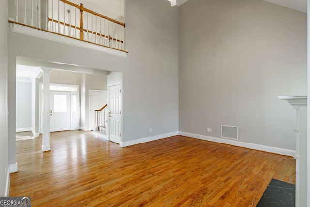 unfurnished living room featuring baseboards, visible vents, wood finished floors, a high ceiling, and ornate columns