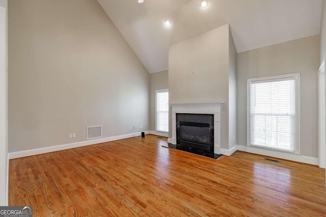 unfurnished living room featuring light wood-style floors, a fireplace with flush hearth, high vaulted ceiling, and baseboards