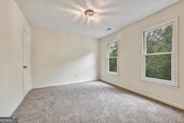 spare room featuring a textured ceiling, carpet flooring, visible vents, and baseboards