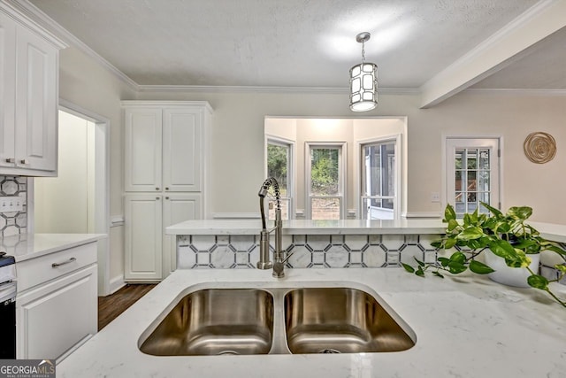 kitchen with light stone counters, white cabinetry, a sink, and decorative backsplash