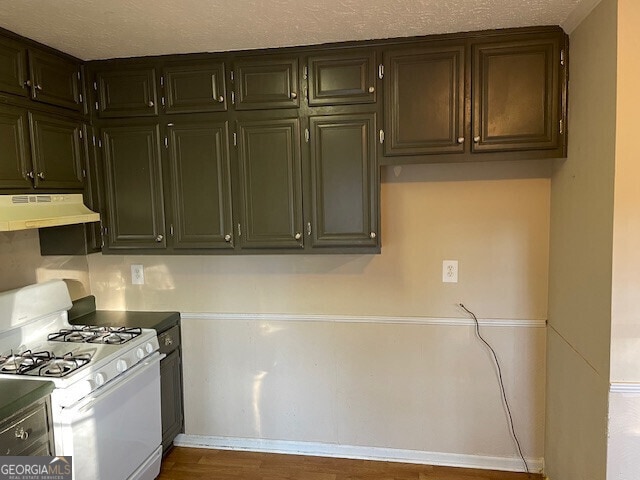 kitchen featuring wood finished floors, under cabinet range hood, a textured ceiling, and white gas range