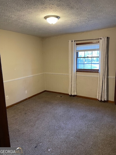 unfurnished room with carpet, visible vents, a textured ceiling, and baseboards