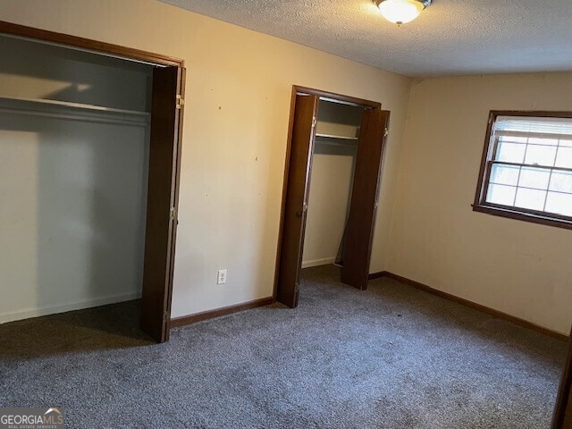 unfurnished bedroom with a textured ceiling, carpet, and baseboards