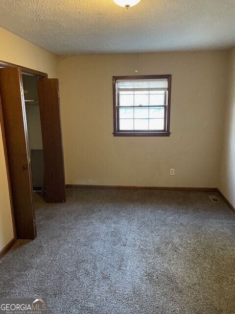 unfurnished bedroom featuring a textured ceiling, carpet floors, a closet, and baseboards