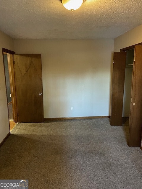 unfurnished bedroom featuring a textured ceiling, carpet floors, a closet, and baseboards