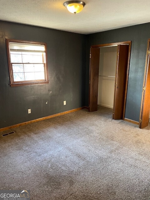 unfurnished bedroom featuring visible vents, baseboards, carpet, a textured ceiling, and a closet