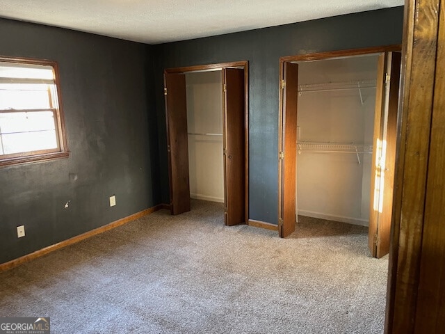 unfurnished bedroom with carpet flooring, baseboards, and two closets