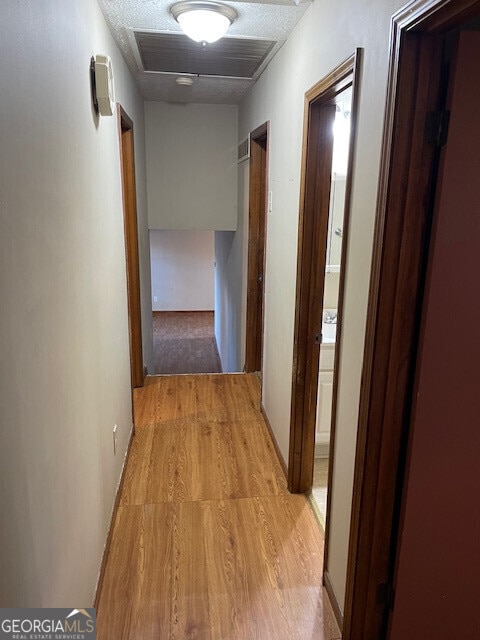 hall featuring light wood-type flooring, attic access, visible vents, and a textured ceiling