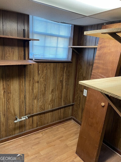 interior space featuring a drop ceiling, wood finished floors, and wooden walls