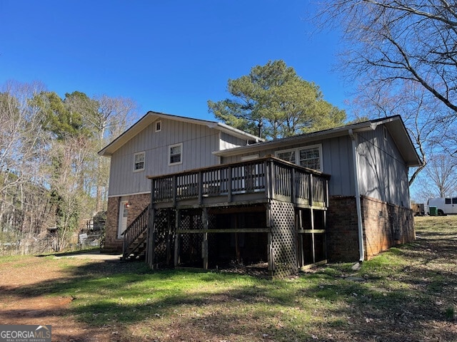 rear view of house with brick siding, a lawn, a deck, and stairs