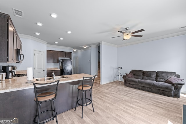 kitchen featuring light wood-style flooring, freestanding refrigerator, a peninsula, dark brown cabinets, and a sink