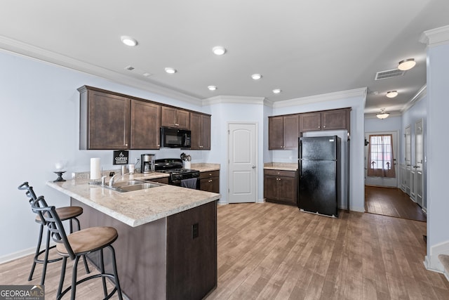 kitchen with dark brown cabinetry, light wood finished floors, light countertops, black appliances, and a sink