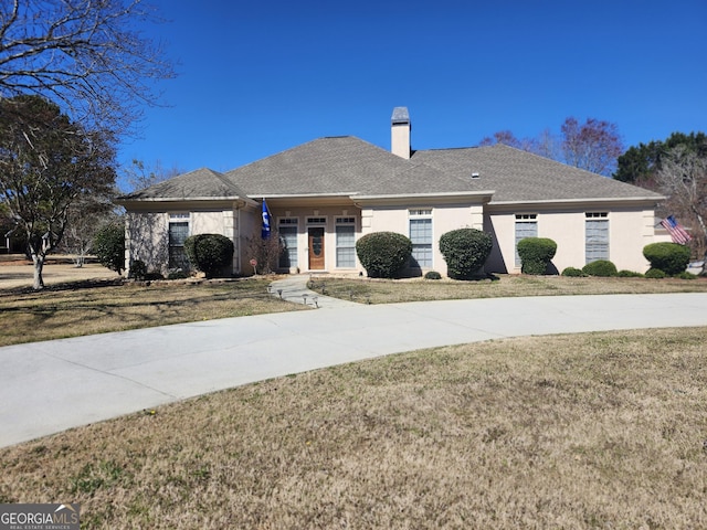 single story home featuring stucco siding, a chimney, a front lawn, and a shingled roof