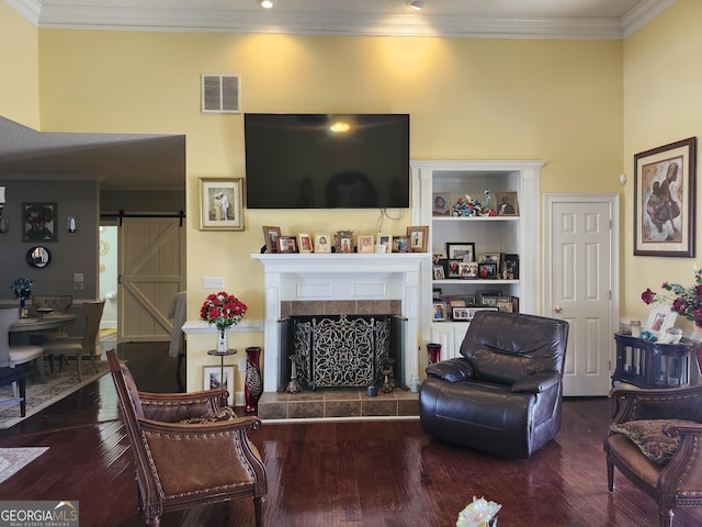 living room with wood finished floors, visible vents, crown molding, a tiled fireplace, and a barn door