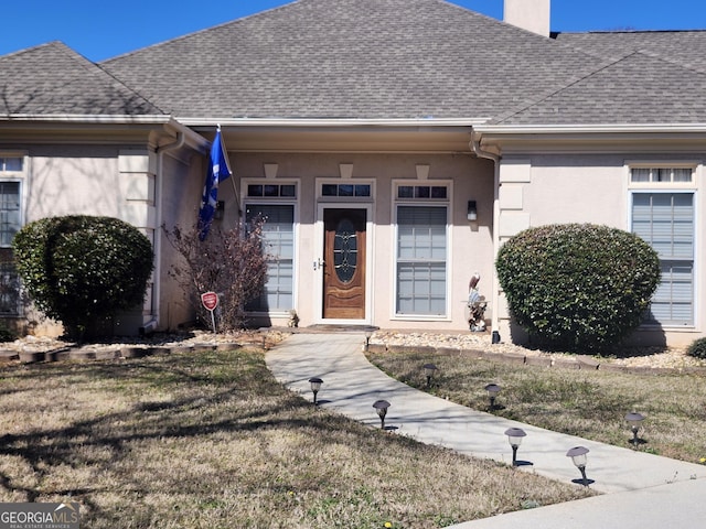 view of front of property featuring a chimney, stucco siding, a shingled roof, and a lawn