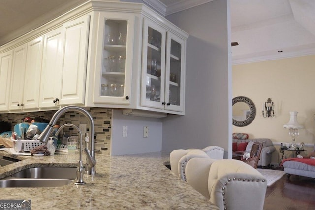 kitchen with light stone countertops, ornamental molding, a sink, glass insert cabinets, and tasteful backsplash