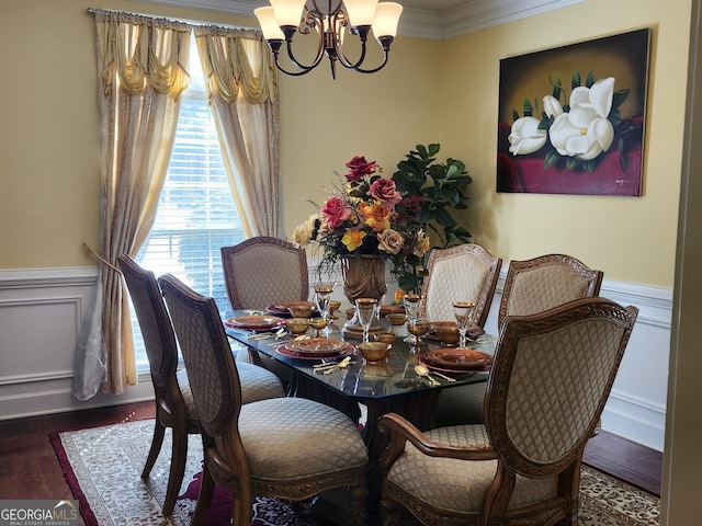 dining room with crown molding, a chandelier, a wainscoted wall, wood finished floors, and a decorative wall