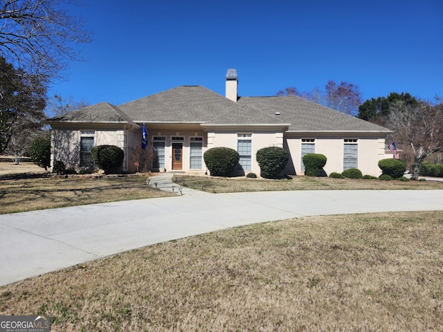 single story home featuring stucco siding, a chimney, and a front yard