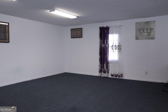 empty room with dark carpet, a textured ceiling, and baseboards