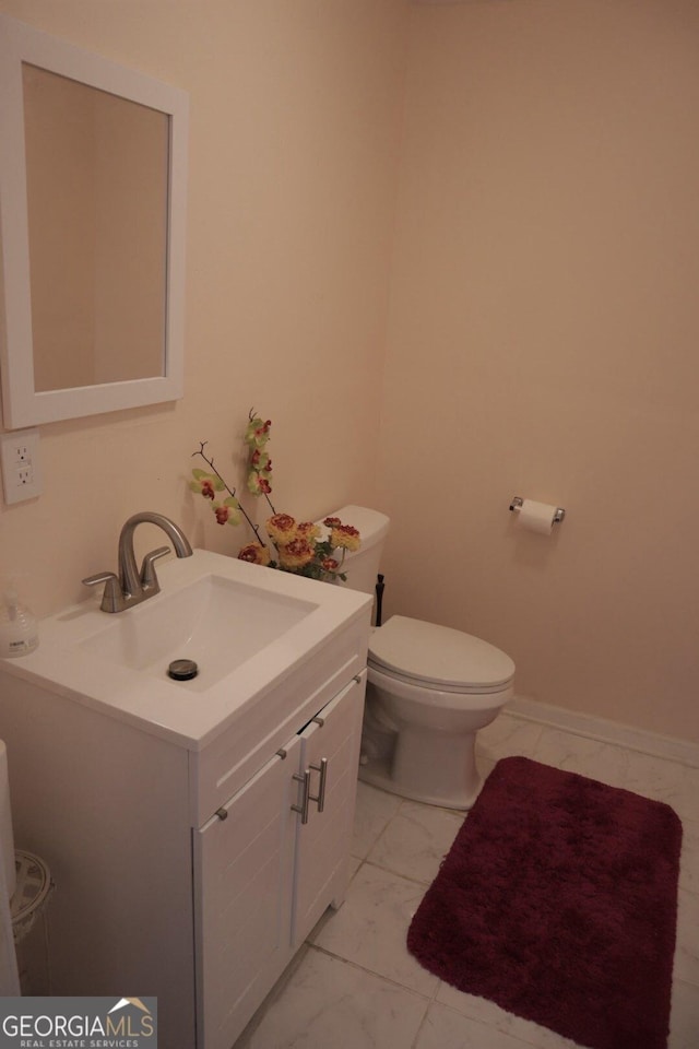 half bathroom with baseboards, toilet, and vanity