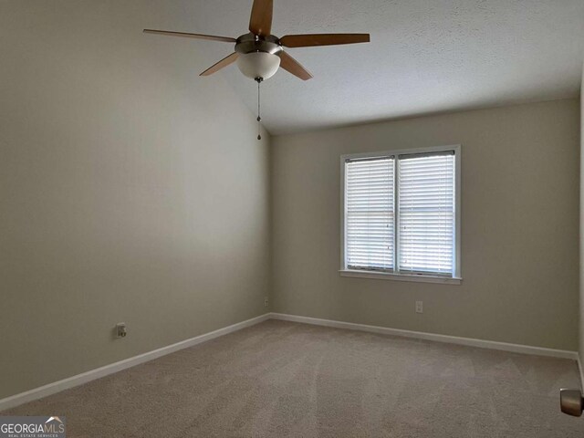 empty room with vaulted ceiling, light colored carpet, ceiling fan, and baseboards