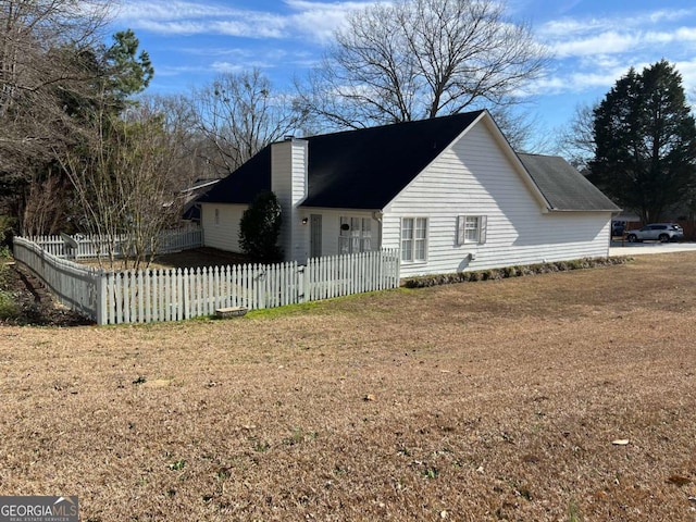 view of property exterior featuring a fenced front yard, a chimney, and a lawn