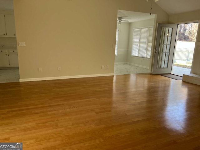 unfurnished living room featuring lofted ceiling, ceiling fan, baseboards, and light wood-style flooring