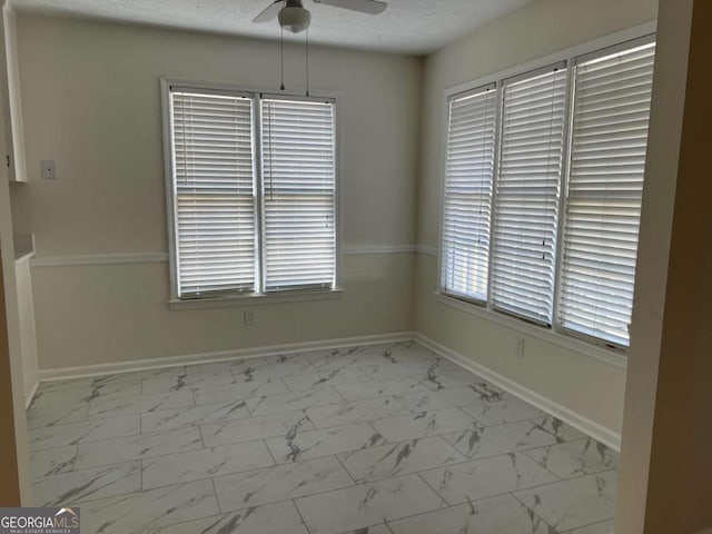 unfurnished dining area featuring a textured ceiling, marble finish floor, ceiling fan, and baseboards