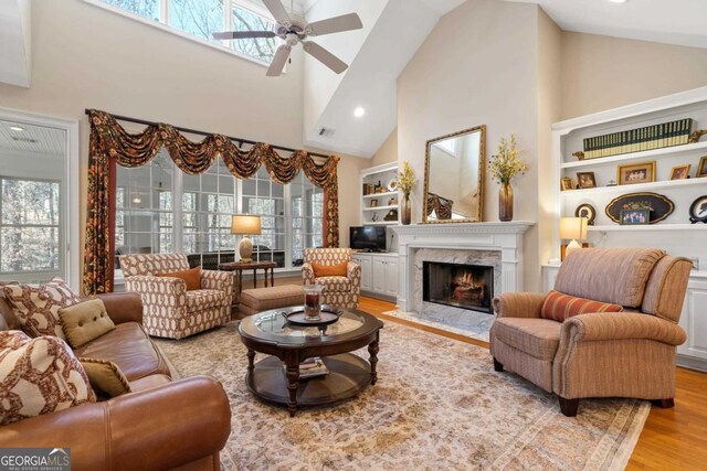 living area featuring a fireplace, visible vents, light wood-style flooring, ceiling fan, and high vaulted ceiling