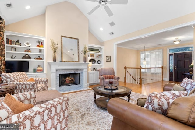 living room with built in shelves, a premium fireplace, wood finished floors, and visible vents