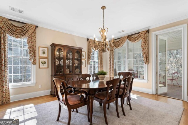 dining room with ornamental molding, light wood-type flooring, visible vents, and an inviting chandelier