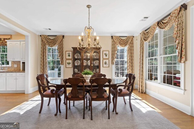 dining space featuring ornamental molding, light wood-type flooring, visible vents, and an inviting chandelier