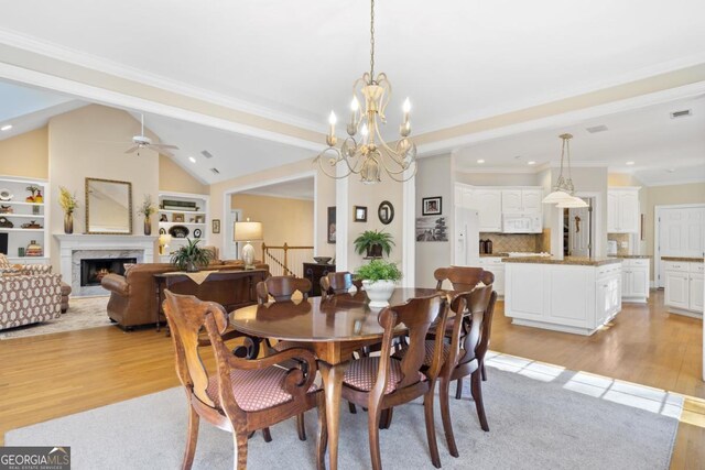 dining room with a warm lit fireplace, visible vents, lofted ceiling, ornamental molding, and light wood-type flooring