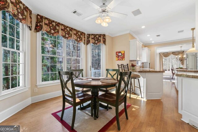 dining space featuring visible vents, ornamental molding, light wood-type flooring, baseboards, and ceiling fan with notable chandelier