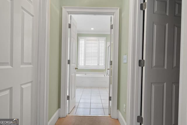 hall featuring light tile patterned floors, baseboards, and crown molding