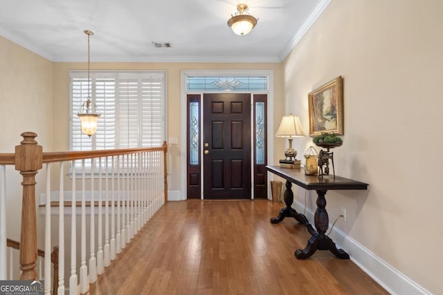 foyer with baseboards, visible vents, ornamental molding, and wood finished floors