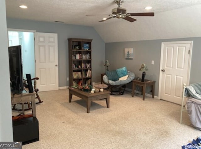 living area featuring lofted ceiling, ceiling fan, a textured ceiling, and light colored carpet