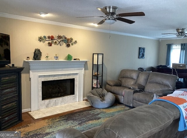 living area featuring a ceiling fan, crown molding, a fireplace, and wood finished floors