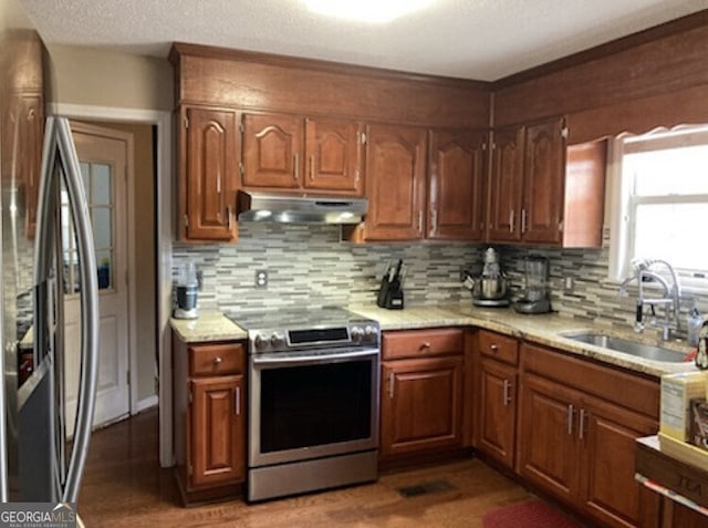 kitchen with decorative backsplash, appliances with stainless steel finishes, wood finished floors, under cabinet range hood, and a sink