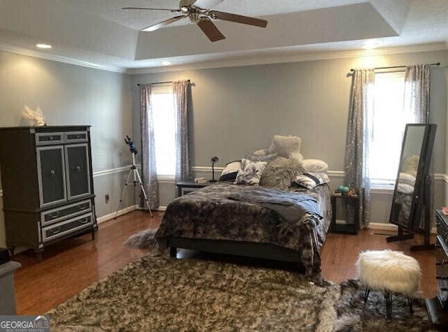 bedroom with crown molding, a raised ceiling, ceiling fan, wood finished floors, and baseboards