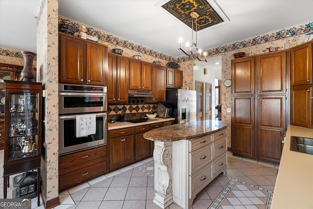 kitchen with wallpapered walls, light tile patterned floors, appliances with stainless steel finishes, and a chandelier