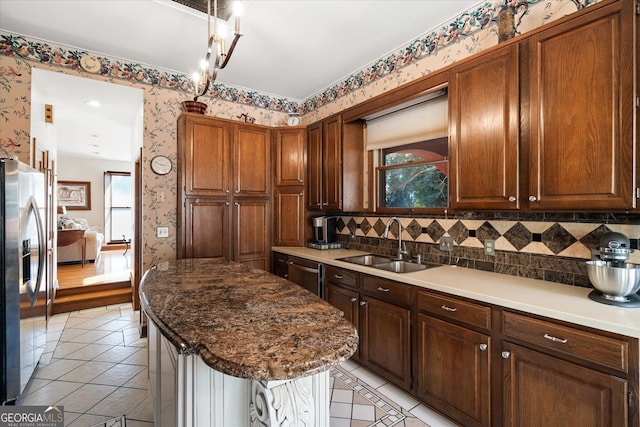 kitchen with light tile patterned floors, stainless steel appliances, a kitchen island, a sink, and wallpapered walls