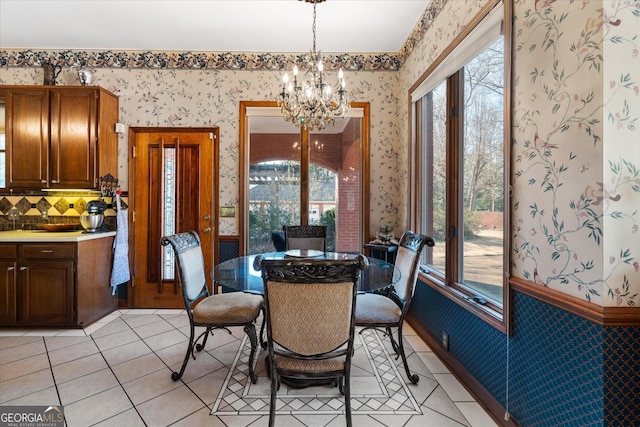 dining area featuring wallpapered walls, light tile patterned floors, a chandelier, and wainscoting