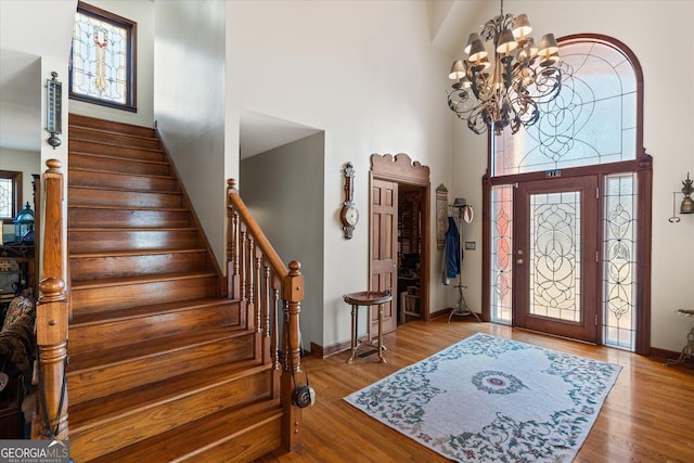 entrance foyer with a chandelier, a high ceiling, wood finished floors, baseboards, and stairs