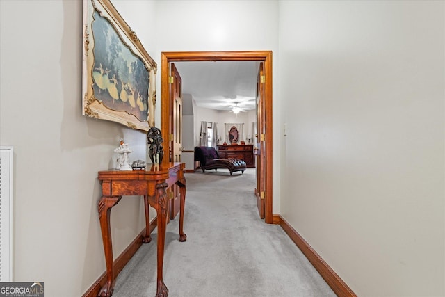 hall with baseboards and light colored carpet