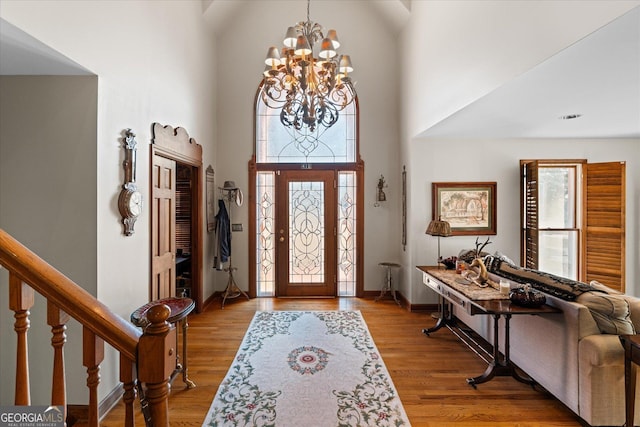 foyer featuring baseboards, wood finished floors, a high ceiling, stairs, and a notable chandelier