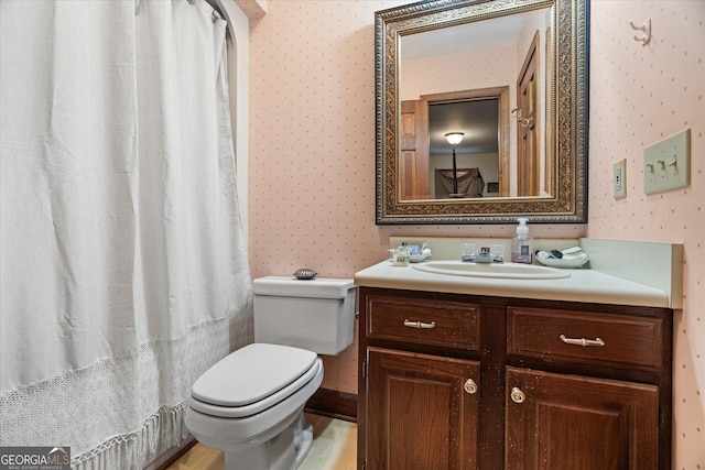 bathroom with vanity, toilet, and wallpapered walls