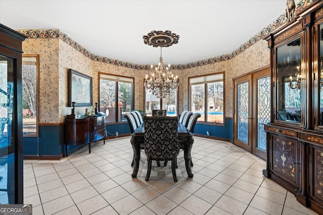 dining area featuring light tile patterned flooring, a notable chandelier, a wainscoted wall, a healthy amount of sunlight, and wallpapered walls